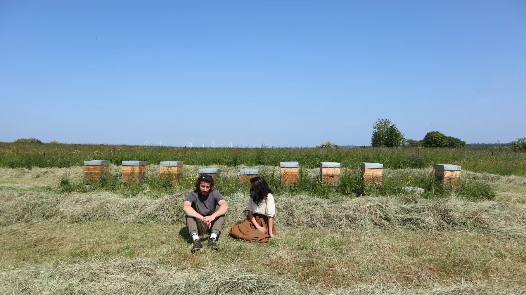 Louis et Galhia assis dans l’herbe devant une rangée de ruches.