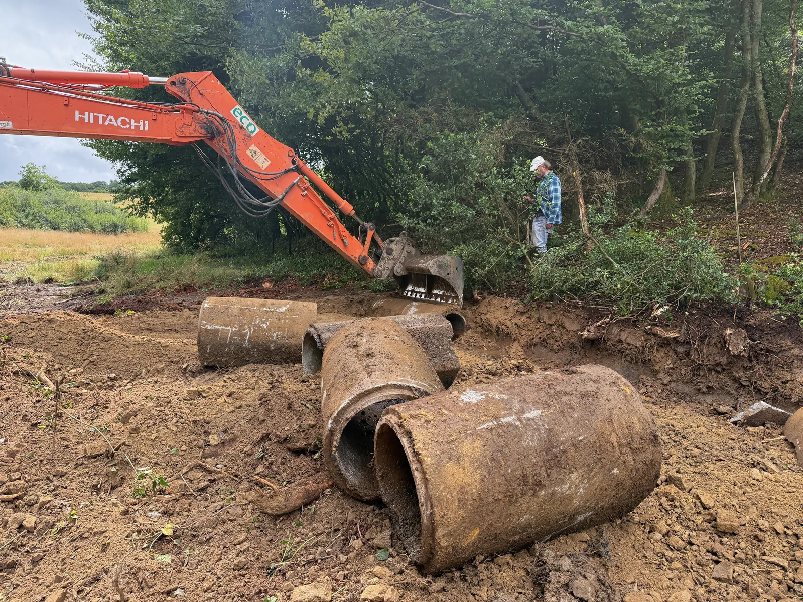 Les grandes buses en béton retirées du ruisseau sont alignées près de la pelleteuse.