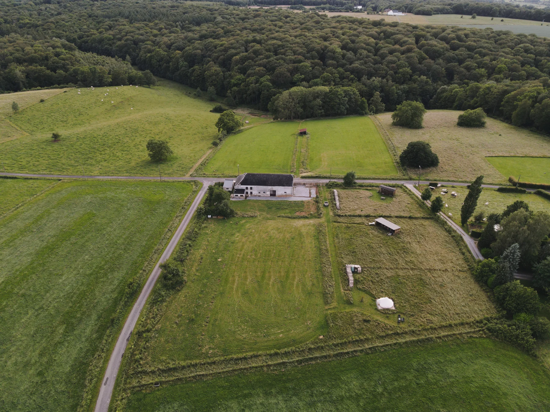 Vue drone de La roulotte ruche : la ferme, les prairies et les hébergements, en lisière de forêt